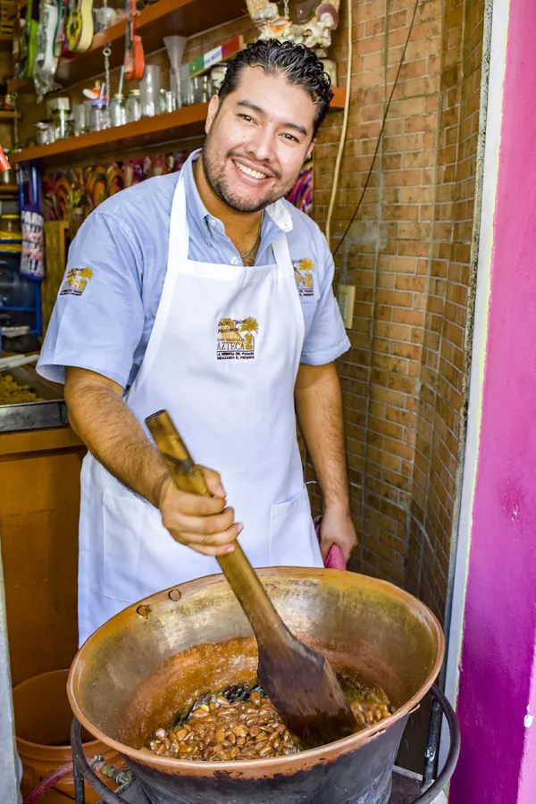 Artesano mexicano sonriente preparando dulces artesanales en un gran cazo de cobre.